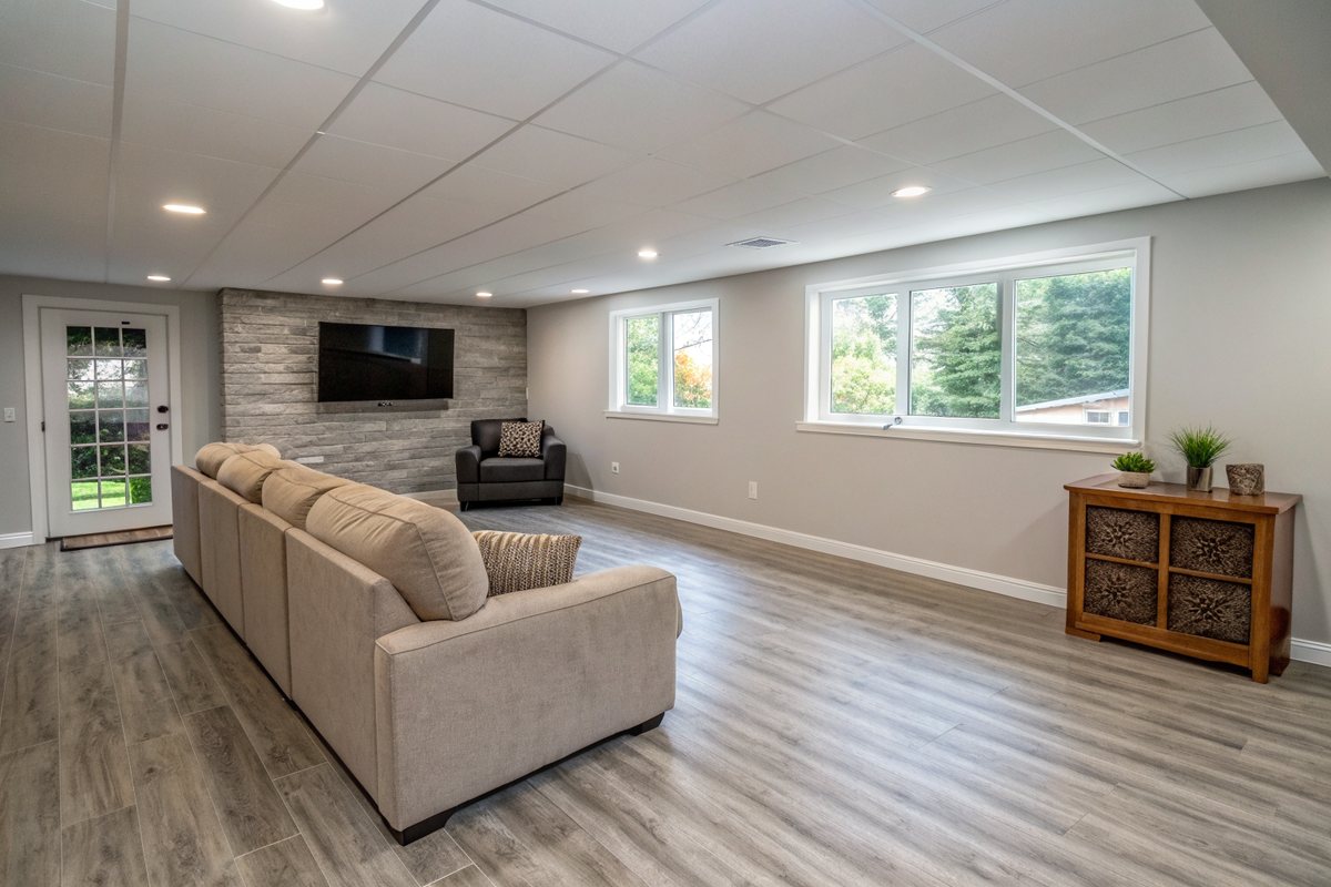 A bright finished basement family room with plank flooring, a sectional sofa and daylight windows